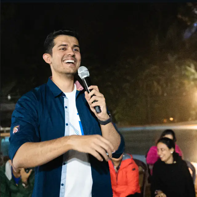 Swastik Nandakumar speaking into a microphone at an outdoor evening session