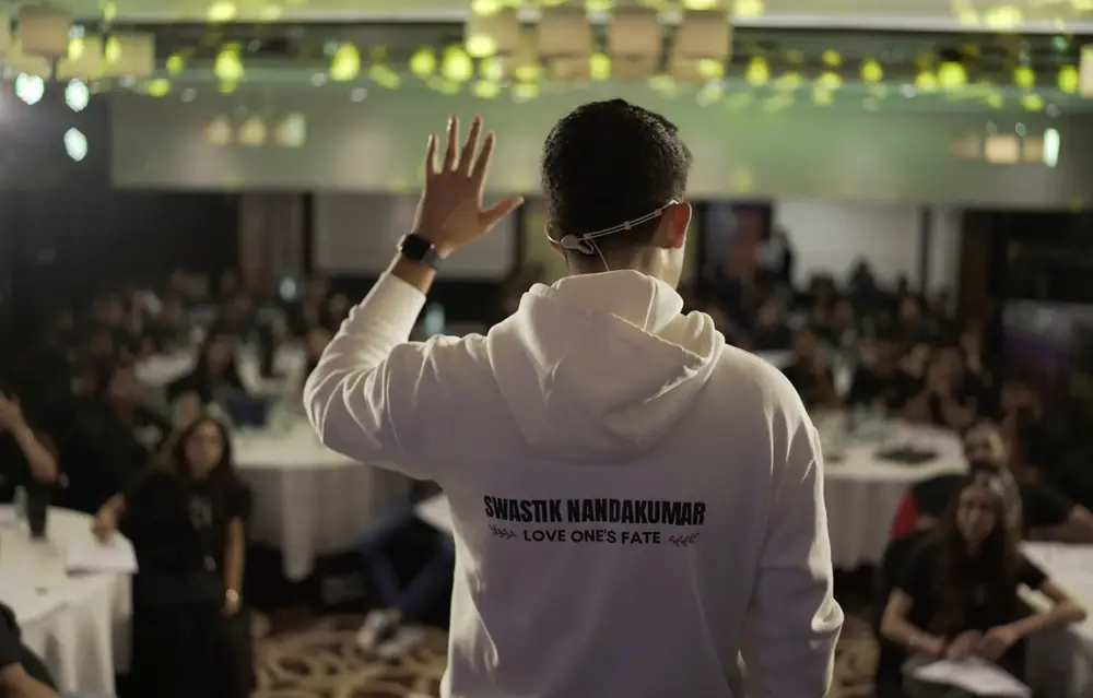 Swastik Nandakumar addressing a full room in a Love One's Fate hoodie